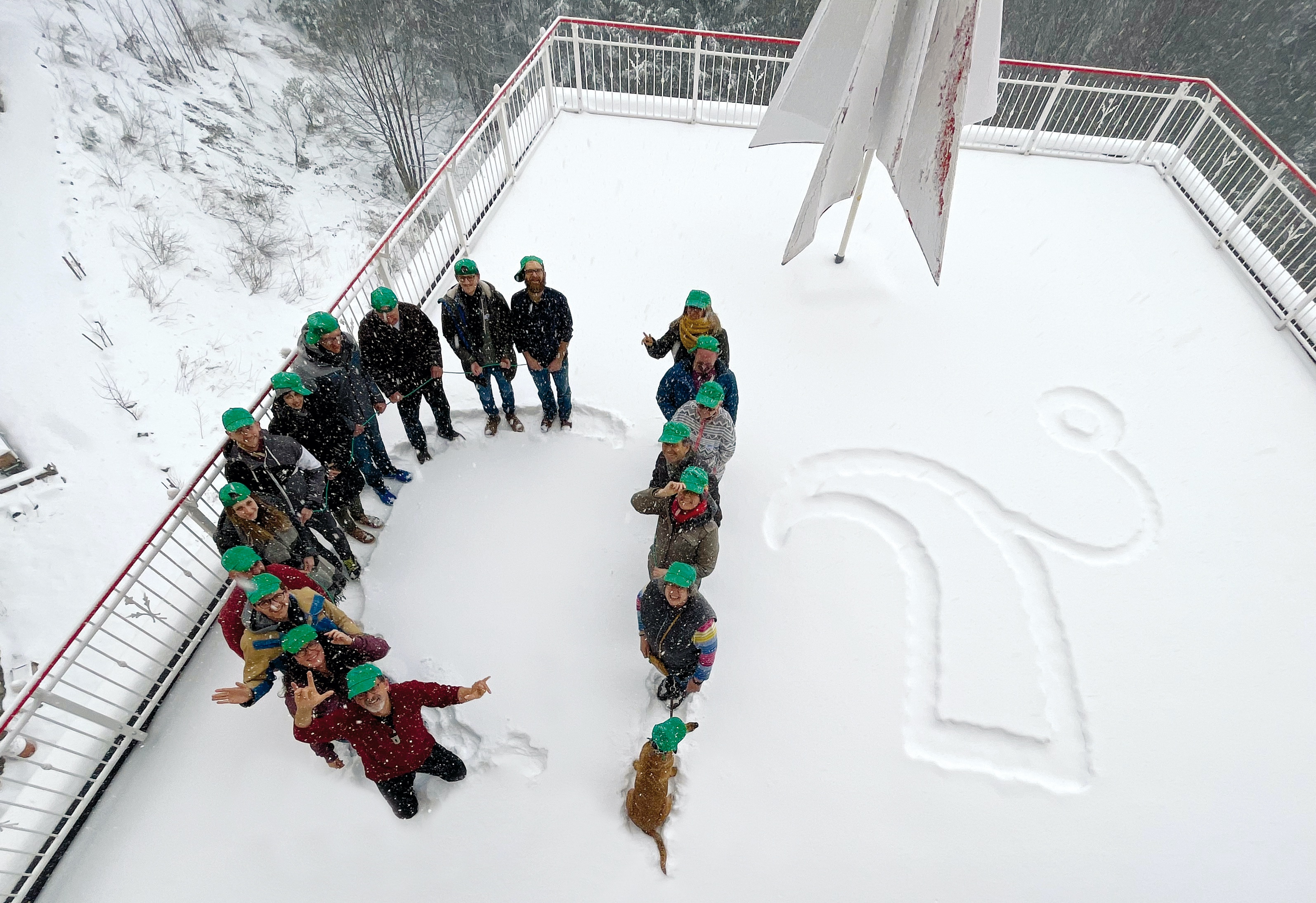 Menschen mit grünen Mützen von oben im Schnee stehend fotografiert. Sie stehen so, dass ihre Körper 